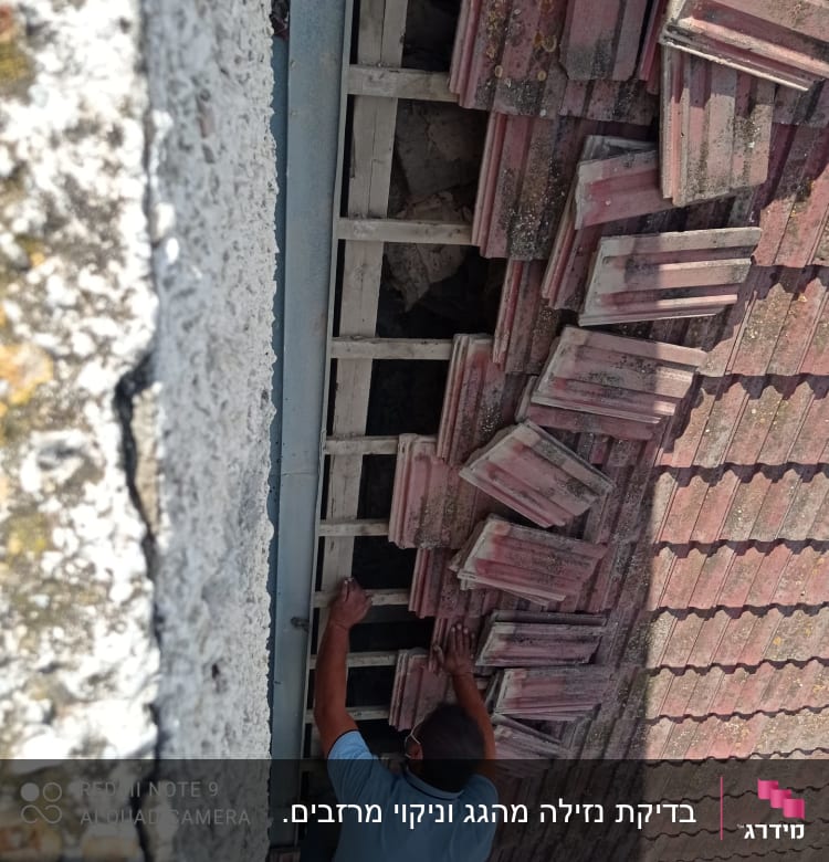 אדם מתקן רעפים על גג שבור